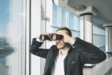 Business man looking with binoculars over panoramic windows