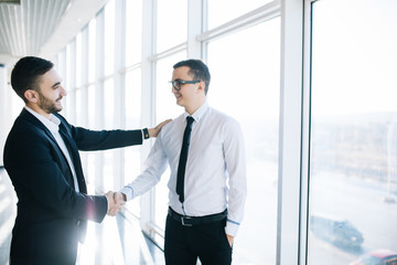 Great job! Two cheerful business men shaking hands and smiling in the background