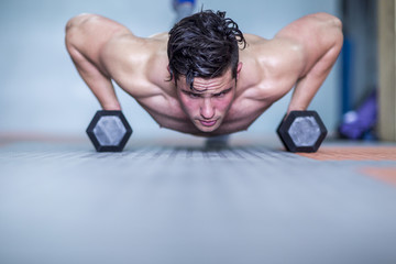 Young man doing dumbbell press ups in gym