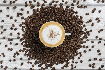 Coffee beans and a cup of Cappuccino in the center of image. Coffee background or texture concept.