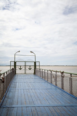 Obraz premium Blue wooden pier on a river. Closed gates decorated with anchors