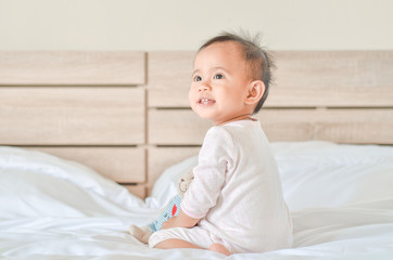 Cute asian baby girl sitting on the bed and playing with a toy b