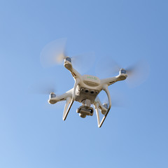 white drone hovering in a bright blue sky