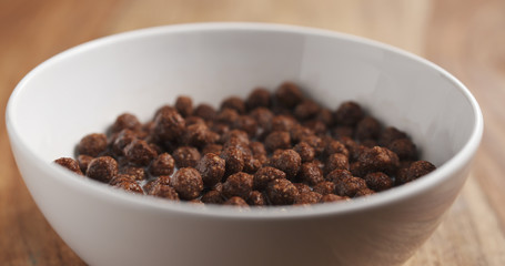 closeup of cereal chocolate balls with milk in white bowl on wood table, 4k photo