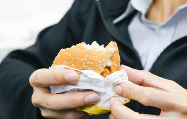 Man is holding a hamburger which already been bitten in hand
