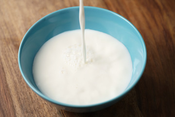 fresh milk poured into blue bowl on wood table, organic food