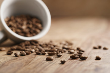 overturned cappuccino cup with roasted coffee beans on wood table, with copy space