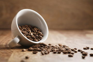 overturned cappuccino cup with roasted coffee beans on wood table, with copy space