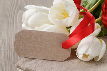 white tulips on wood table with paper tag for yout text