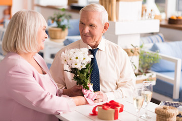 Gallant grey haired man presenting his lady flowers