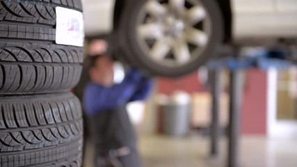 Horizontal slide shot of a stack of new tires in a service station garage with a mechanic working on a car on the lift in the background.
