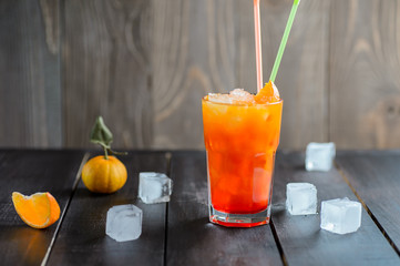 Fresh orange cocktail drink with ice cubes on black wooden background