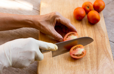 Hand with knife cutting fresh red tomatoes on on cutting board