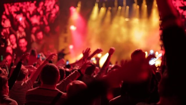 Crowd waving hands and phones at live music concert, slow-motion