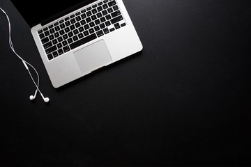 Laptop and earbuds on dark, black desk