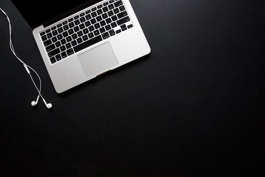 Laptop and earbuds on dark, black desk
