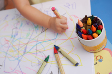 Fototapeta premium Hand of baby drawing lines on the white paper with colorful crayons. Focusing at the box of crayon and blur other part. 