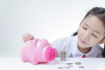 Asian little girl in Thai student uniform putting coins to piggy