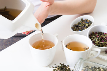Woman poured hot green tea into cups and different kind of herbs