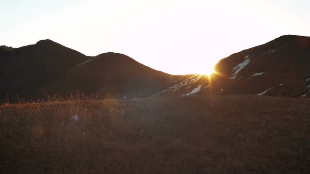 Sun rising from behind snow mountains. Tight shot with a beautiful lens flare moves through frame