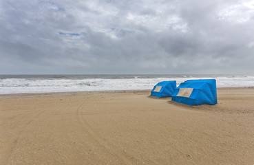 Two blue wind tent shelters on stormy beach. Horizontal.