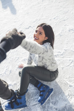 Young and beautiful woman enjoying in ice skating. She gets help after the fall.