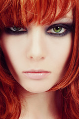 Vintage style close-up portrait of young beautiful green-eyed girl with red hair and stylish smoky eyes makeup