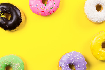 Pink round donut and few other on yellow background. Flat lay, top view.