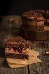 A piece of tasty holiday chocolate homemade cake with cream fruit filling and chocolate topping, it is on the old textured wooden table and paper.