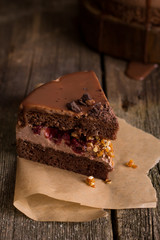 A piece of tasty holiday chocolate homemade cake with cream fruit filling and chocolate topping, it is on the old textured wooden table and paper.