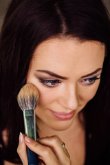 Make-up artist hand applying bright base color on model's face and holding a brush , close .