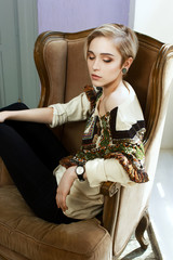 Beautiful girl in a clothes with an ethnic pattern, sitting in a chair in front of a window