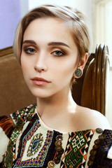 Beautiful girl in a clothes with an ethnic pattern, sitting in a chair in front of a window