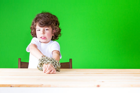 Curly sad boy tries to free chain bound hands and looking into the camera. Close-up. Green background.