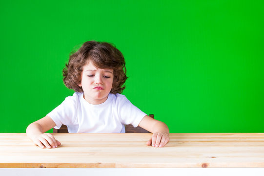 The curly-haired pretty boy sticking out his mouth sitting at a desk crying. Close-up. Green background.