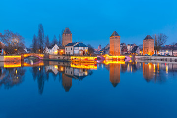 Fototapeta na wymiar Medieval towers and bridges Ponts Couverts with mirror reflections in Petite France during twilight blue hour, Strasbourg, Alsace, France
