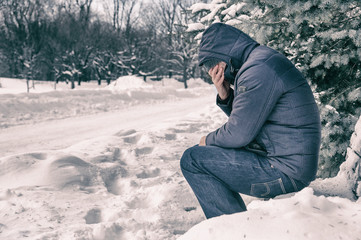 Man sitting on bench in a forest in winter with snow on the ground.