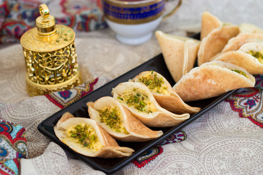 Traditional Arabic qatayef crepes stuffed with cream and pistachios, prepared for iftar in Ramadan on paisley background above