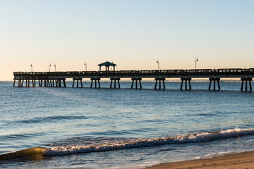 Fototapeta premium Fishing pier with waves at Buckroe Beach in Hampton, Virginia at sunrise.