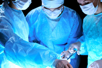 Medical team performing operation. Group of surgeon at work in operating theatre toned in blue.