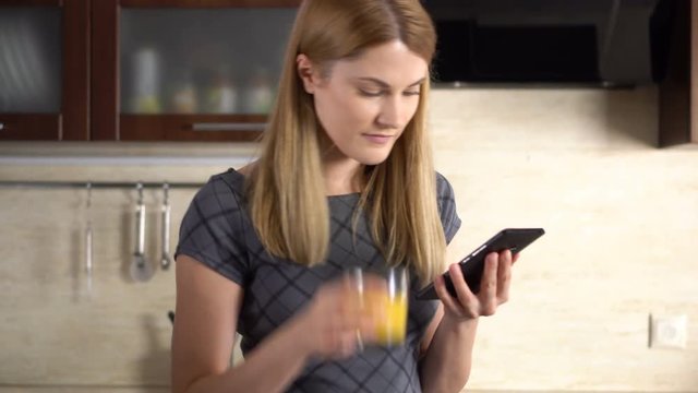 Beautiful young woman with a phablet standing in kitchen. Browsing Internet and smiling.