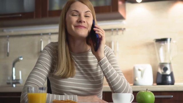 Beautiful attractive casual young woman sitting in a kitchen and talking on the phone with a friend.