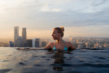 Young woman in a roof top swimming pool with beautiful city view. Vacation in Singapore 
