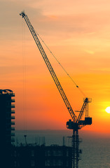 Silhouette of construction tower crane with sunset background at evening time.