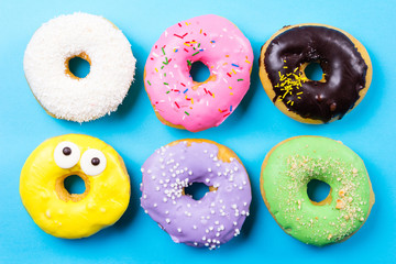 Colorful round donuts on blue background. Flat lay, top view.