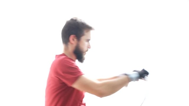 Profile of young bearded determined man working out hard on the rowing machine, studio isolated on white background.