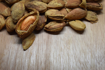 Pile of dry almond nuts spread out on wooden surface and empty space for text.