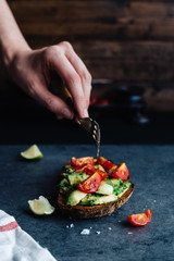 Female Hand with Fork Eating Avocado and Cherry Tomatoes on Toast
