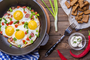 Fred eggs in pan with tomatoes and green fresh onion.
