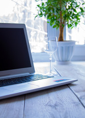 Laptop, empty glass and ficus in the background of a winter window